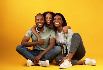 Family portrait. Happy african american parents and their daughter hugging and smiling, sitting on yellow background