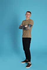 Young man with tattoos on light blue background