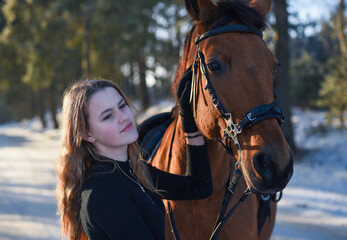 Obraz premium Young girl with horse on winter forest road