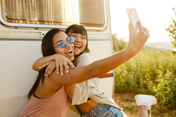 Multiracial two women hugging while taking selfie on cellphone