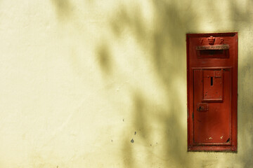 An old and dysfunctional red letterbox built into a ruggedly plastered wall