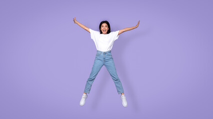 Fototapeta na wymiar Carefree Aisan Young Lady Jumping Spreadeagle Over Purple Studio Background