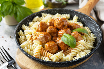 Italian  kitchen. Italian fusilli pasta with meat balls in tomato sauce and basil on grey stone background.