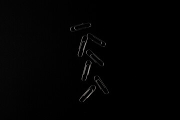 Metal paper clips lie on a black background