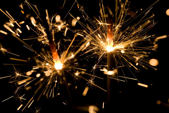 Selective focus, sparkling close-up of two gold, glowing, sparklers on a black background creates an abstract, bokeh texture. Full frame, extreme close-up.
