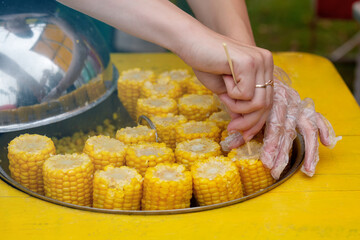 Boiled ripe corn cob with salt close-up, photo with a human hand, take one. A woman's hand holds freshly cooked yellow corn. Seasonal street trading