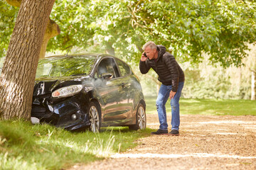 Fototapeta Mature Man Next To Car Crashed Into Tree Inspecting Accident Damage And Calling Emergency Services obraz