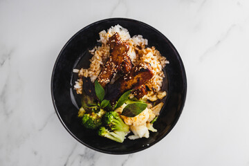 vegan marinated teriyaki tempeh withsteamed broccoli and coauliflower on a bed of white coconut...