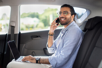 Positive indian man freelancer working online while sitting in taxi