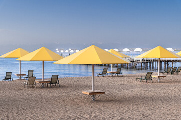 Seascape with sandy beach, umbrella and deck chairs. Design of summer vacation holiday