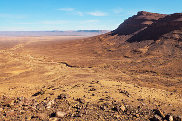 Fototapeta na wymiar Flat large rocky canyon basin with clear sky above - typical landscape in Southern Morocco