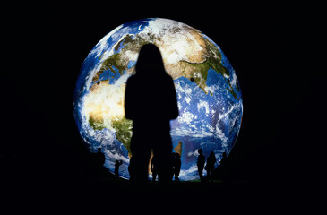 Silhouettes of people and young woman standing in front of large inflatable model of planet Earth...