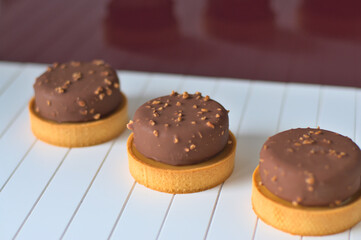 Round sweet delicious tarts covered with milk chocolate with nut pieces