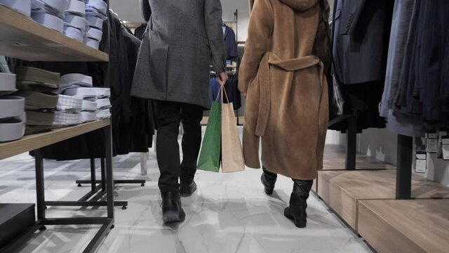 Close up couple legs walking down clothing store with shopping bags. Man and woman returns from the mall dressed in winter clothes carries bags of gifts shopping, modern family spends time together.