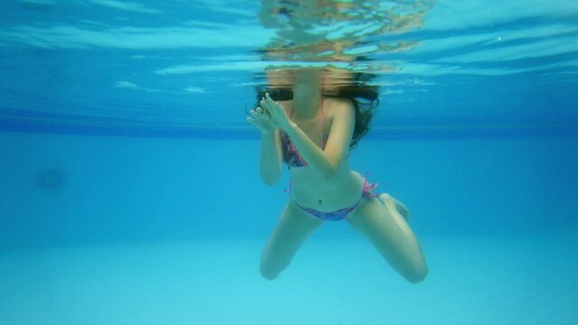 Relaxed woman swimming at pool, underwater shot. She stroke water by hands and kick legs, move towards camera. Tourist lady recreate at large wading pool