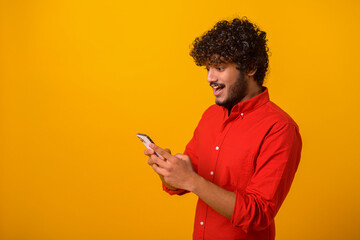 Portrait view of young adult man looking at mobile phone with shocked astonished expression with...
