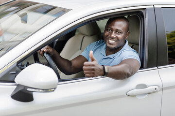 Happy black man driving luxury white car, showing thumb up
