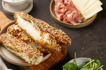 Savoury breakfast ingredients: brown lye bread sticks garnished with oats , pork slices prosciutto, hard cheese gouda and fresh greens on wooden boards