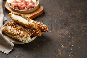 Savoury breakfast ingredients: brown lye bread sticks garnished with oats , pork slices prosciutto,...
