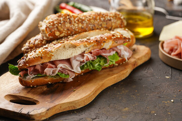 Long sandwich in brown lye bread sticks garnished with oats , pork slices prosciutto, hard cheese gouda and fresh greens on wooden boards