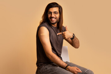 Handsome indian man got vaccinated, pointing at shoulder with plaster