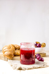 Plum jam in a glass jar. Plum jam, croissants and ripe plums in the background.