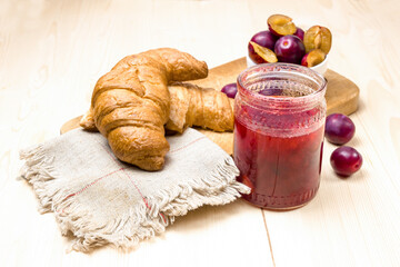 Plum jam in a glass jar. Plum jam, croissants and ripe plums in the background.