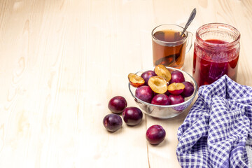 Home made plum jam in a glass jar. Black tea. Plum jam and ripe plums. Checkered towel. High key.