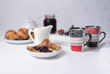Desayuno con croissants, café y mermelada de higos sobre una mesa con fondo blanco