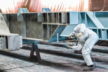 The painter is working to painting the steel structure with spray gun at industrial factory