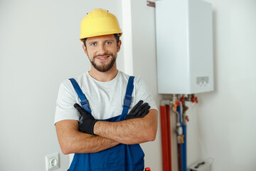 Cheerful male worker, technician servicing the house heating system smiling at camera while standing with arms crossed