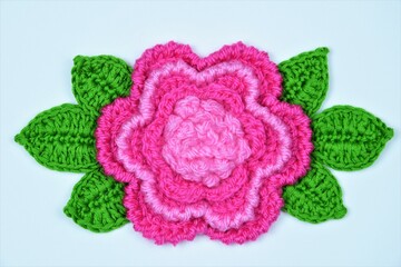 Crocheted flower and leaves on a white paper background

