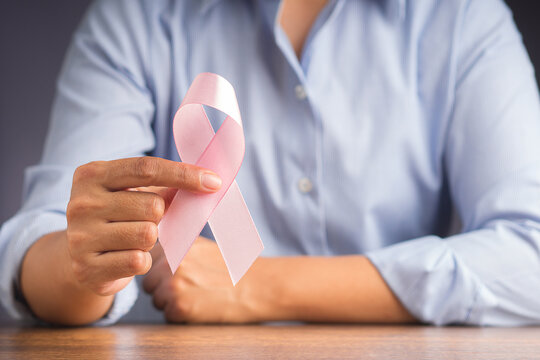 Woman in a blue shirt with hand holding pink ribbon for cancer patients support. Breast cancer awareness concept