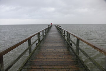 Fototapeta premium Wooden pier leading into the North Sea during high tide on a rainy day (horizontal image), Burhave, Lower Saxony, Germany