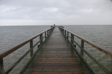 Wooden pier leading into the North Sea during high tide on a rainy day (horizontal image), Burhave,...