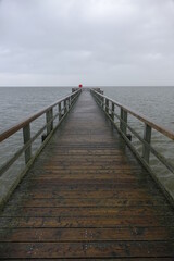 Wooden pier leading into the North Sea during high tide on a rainy day (vertical image), Burhave, Lower Saxony, Germany
