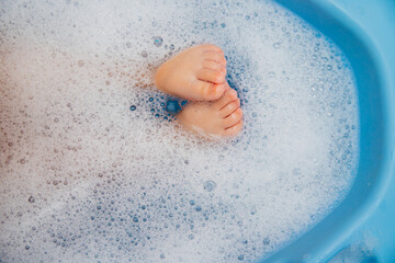 Baby feet in a blue bubble bath. Baby detergent, hygiene. Baby skin care. Background, texture of soap bubbles.
