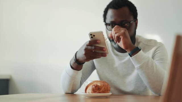Concentrated African man looking at phone at breakfast at home