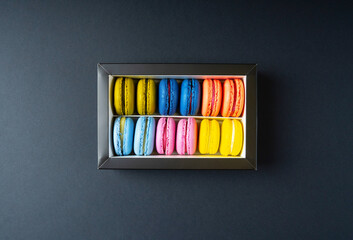 Macaroons top view. Colorful macaroons cookies in a paper box on a black background.