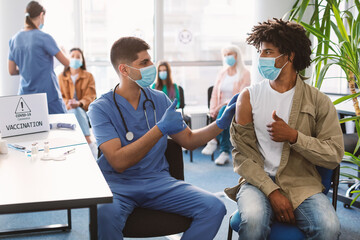 Vaccinated Black Guy And Doctor Gesturing Thumbs-Up At Clinic - obrazy, fototapety, plakaty
