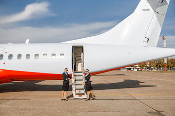 Flight attendants standing near airplane and inviting on board