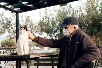 Man in mask strokes cute stray homeless cat on street. Selective focus.