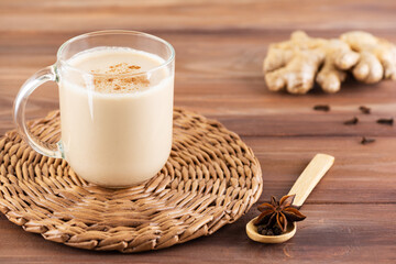 Masala chai with coconut milk and spices in a glass mug on a wooden table. Selective focus.