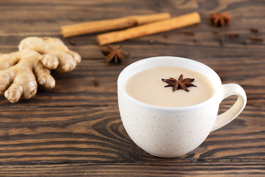 Masala chai with coconut milk, anise, cinnamon, ginger, pepper in a cup on a wooden table. Selective focus.