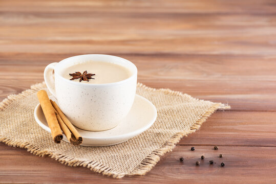 Masala tea with coconut milk and spices in a cup on a wooden table. Selective focus.