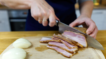 cook cuts bacon on a wooden board. close up