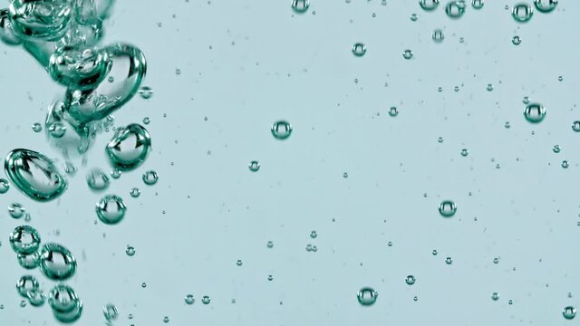 Macro shot of air bubbles in water rising up on light blue background. Slow motion. High quality FullHD footage