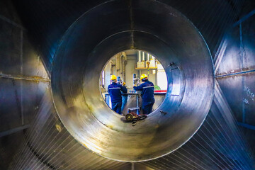 2 men doing work at the end of the metal pipe