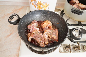 Tasty chicken meat portions in the pan. Frying or roasting processing. Preparing food on a kitchen stove. The classic French delightful dish «Coq au vin». Food background.

