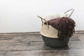Handwoven seagrass belly or blanket basket with handles with beige and brown throws. Trendy natural multifunctional container for storage laundry, grocery, toy, plant in home. Side view, copy space